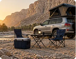 Folding table, two chairs and cool box beside a 4x4 at a wadi campsite